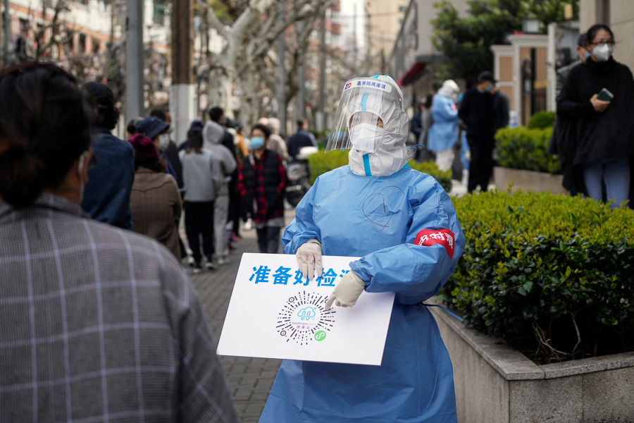 A worker in a protective suit shows a QR code to residents lining up for nucleic acid testing, as the second stage of a two-stage lockdown to curb the spread of the coronavirus disease (COVID-19) begins in Shanghai, China April 1, 2022.  (Credit: Aly Song / Reuters)

