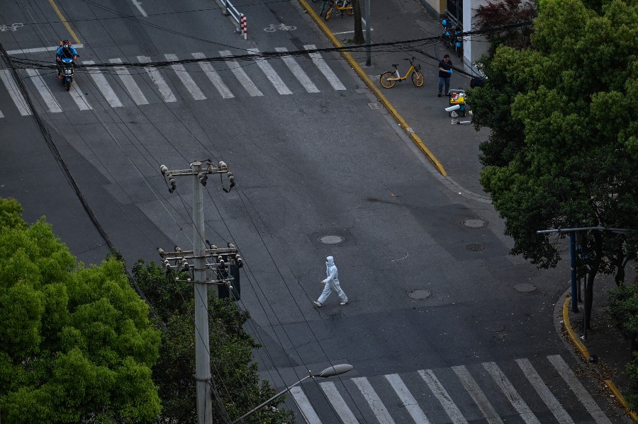 A worker wearing personal protective equipment (PPE) walks on a street during a COVID-19 lockdown in the Jing'an district in Shanghai on April 12, 2022. (Credit: Hector RETAMAL / AFP)