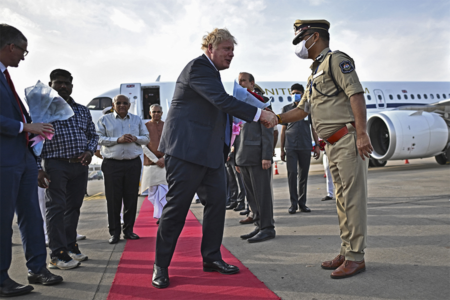 Britain's Prime Minister Boris Johnson (C) is greeted by a police official upon his arrival at the airport in Ahmedabad on April 21, 2022. (Credit: BEN STANSALL / POOL / AFP)