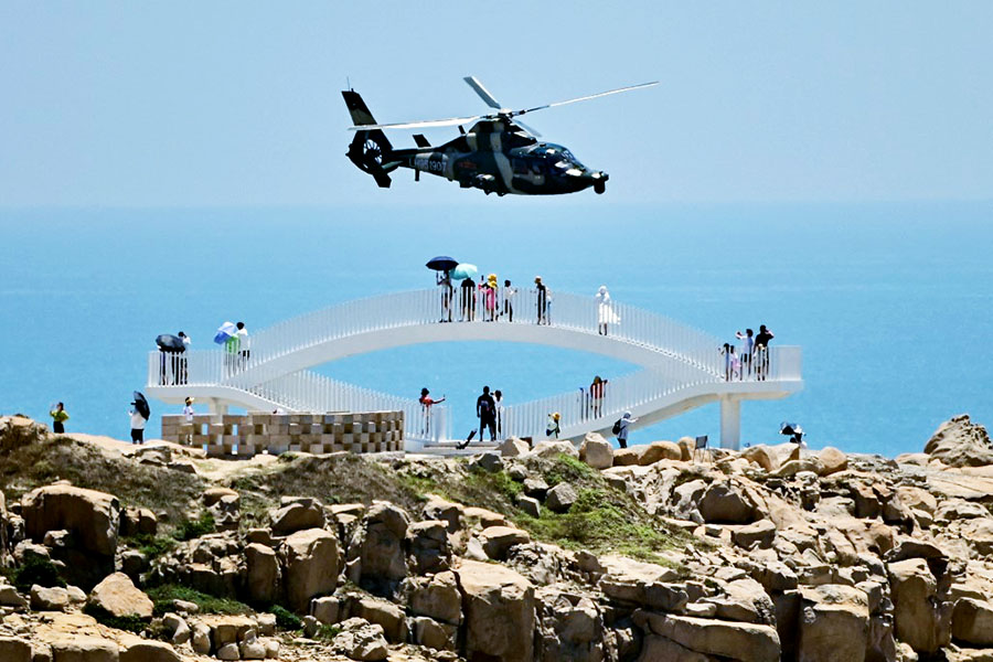 Tourists look on as a Chinese military helicopter flies past Pingtan island, one of mainland China's closest point from Taiwan, in Fujian province, following US House Speaker Nancy Pelosi's visit. Image: Hector Retamal/AFP 
