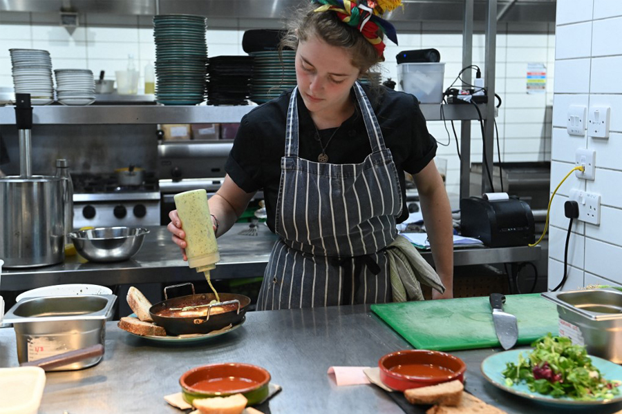 A member of staff prepares some food at The Canteen restaurant, one of the first in the UK to place the carbon footprint of its dishes on its menu besides the calories, in Bristol, on August 3, 2022. Image: Ashley Crowden / AFP