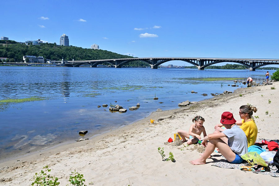 A family sits on the sandy shores of the Dnipro river that runs through the Ukrainian capital of Kyiv on July 2, 2022. Ivan Sukhanov and his family used to holiday by the Black Sea. This summer they are gong no further than the banks of the Dnipro river in the heart of Kyiv. Four months after Russian troops marched into Ukraine in February 