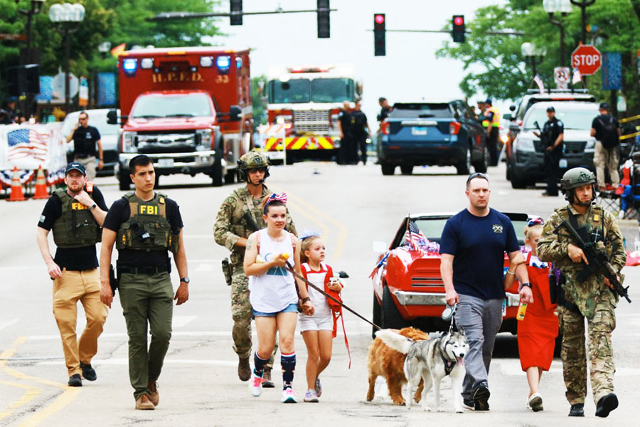 Law enforcement escorts a family away from the scene of a shooting at a Fourth of July parade on July 4, 2022 in Highland Park, Illinois. Police have detained Robert “Bobby” E. Crimo III, 22, in connection with the shooting in which six people were killed and 19 injured, according to published reports. Image: Mark Borenstein / Getty Images via AFP
