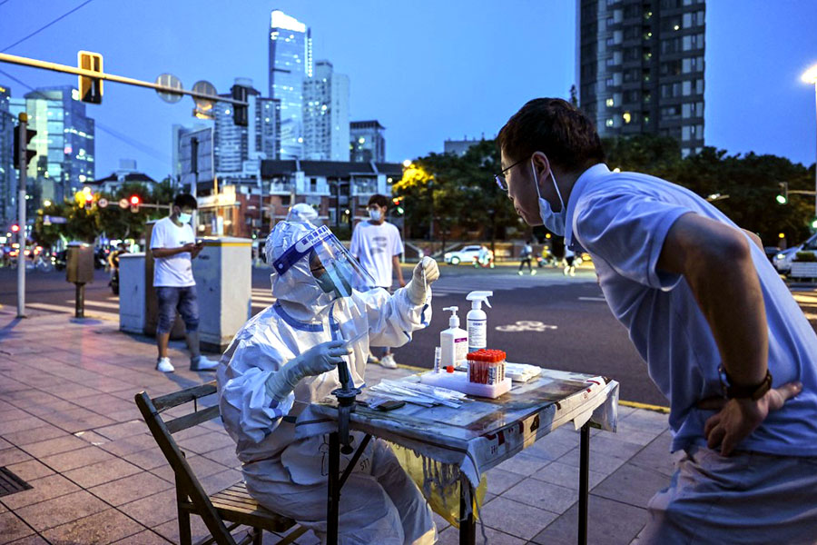 A health worker takes a swab sample from a man to test for the Covid-19 coronavirus on a street next to a residential area in the Jing'an district of Shanghai on July 5, 2022. Image: Hector RETAMAL / AFP 