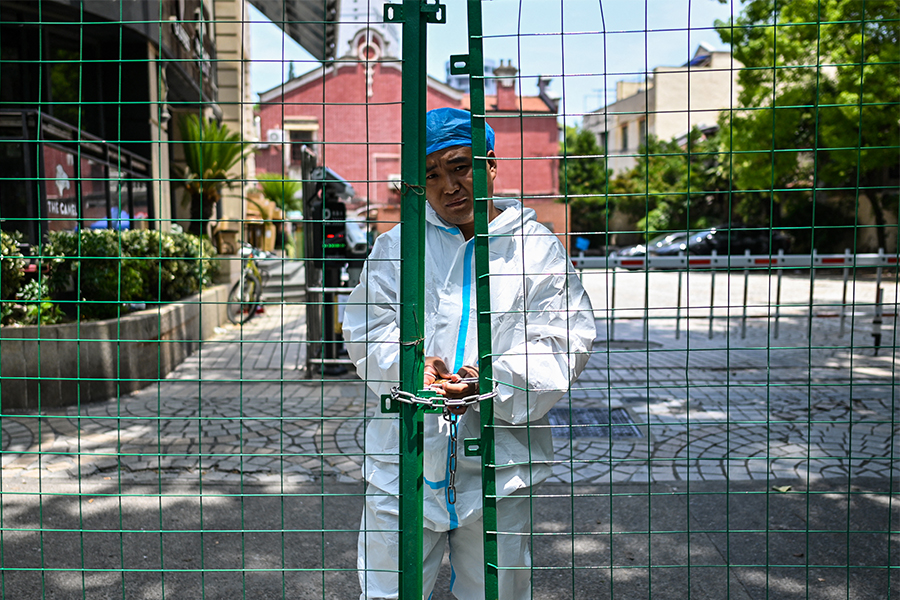 A worker padlocks fencing securing a residential area under Covid-19 lockdown in the Xuhui district of Shanghai on June 8, 2022. Image: Hector Retamal / AFP

