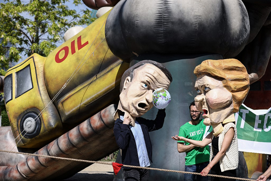 Environmental activists, wearing masks mimicking EU leaders, EU Commission President Ursula von der Leyen and France's President Emmanuel Macron,   protest to call on EU leaders to exit the Energy Charter Treaty (ECT) near the European headquarters in Brussels in May, 2022. Image: Kenzo TRIBOUILLARD / AFP)