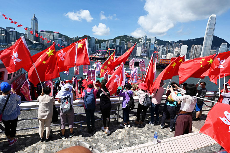 People wave Chinese and Hong Kong flags as fishing boats with banners and flags to mark the 25th anniversary of the Handover of Hong Kong from Britain to China sail through Hong Kong’s Victoria harbour on June 28, 2022. Image: Peter Parks / AFP

