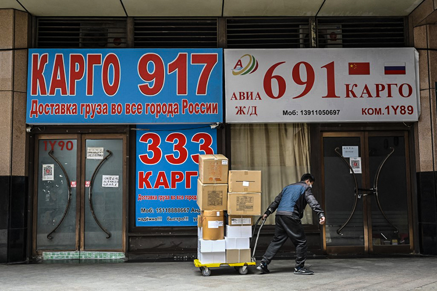 A delivery man hauls packages past stores advertising international logistics transportation to Russia, in Ritan International Trade Center in Beijing on March 22, 2022. Beijing is Moscow's largest trading partner, with trade volumes last year hitting 147 billion USD, according to Chinese customs data, up more than 30 percent on 2019. (Credit: Jade GAO / AFP)