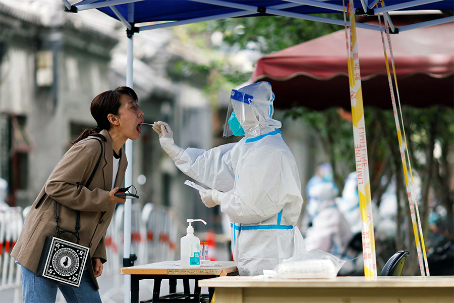A worker in a protective suit collects a swab from a resident at a makeshift nucleic acid testing site amid the coronavirus disease (COVID-19) outbreak, in Beijing, China May 9, 2022. ​(Credits: Carlos Garcia Rawlins/ Reuters)