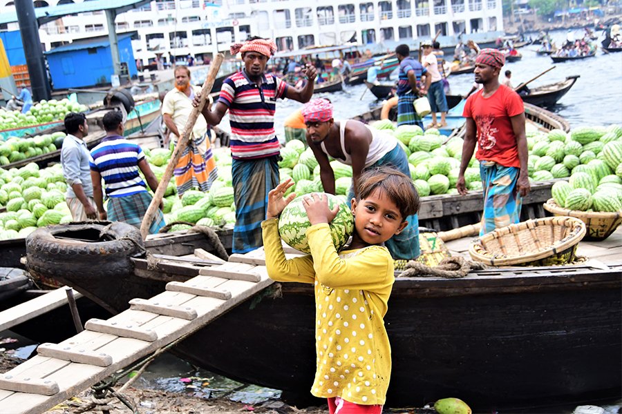 Rupa, 9, who migrated to an urban slum last year after a cyclone destroyed her rural home, unloads watermelons at Sadarghat, a wharf near Dhaka, Bangladesh, March 22, 2022. Image: Thomson Reuters Foundation/Mosabber Hossain
