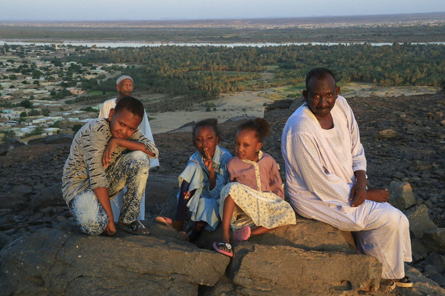 A family poses for a picture on a rock overlooking the Nile River and Karima city in Sudan's Northern State, on October 29, 2022. Climate change, pollution and exploitation by man is putting existential unsustainable pressure on the world's second longest river on which millions of Africans depend. Image: ASHRAF SHAZLY / AFP