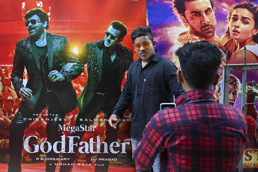 In this picture taken on October 1, 2022, a moviegoer poses for a picture next to a cinema poster of Tollywood star Chiranjeevi and Bollywood's Salman Khan outside the G7 multiplex in Mumbai. India's Bollywood film industry, long part of the cultural fabric of the movie-mad country of 1.4 billion people, is facing its biggest-ever crisis as streaming services and non-Hindi language rivals steal its sparkle. Image: Punit PARANJPE / AFP

