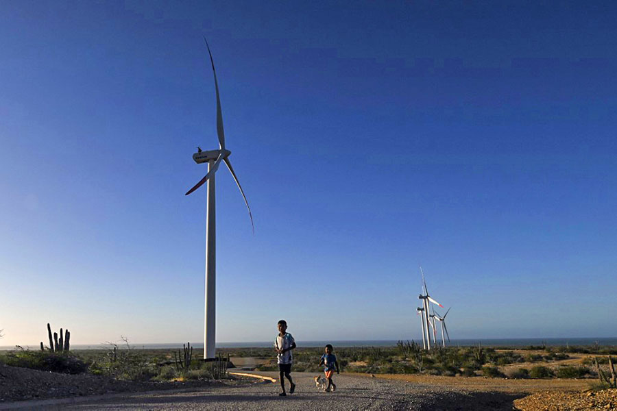 Indigenous Wayuu children walk next to the windmills of the Guajira 1 Eolic Rnergy project near the Cabo de la Vela in Uribia, department of La Guajira, Colombia. Wayuu indigenous are leading a quixotic fight against multinationals that see Colombia's far north as a renewable energy mine. Image: Joaquin Sarmiento/ AFP) 