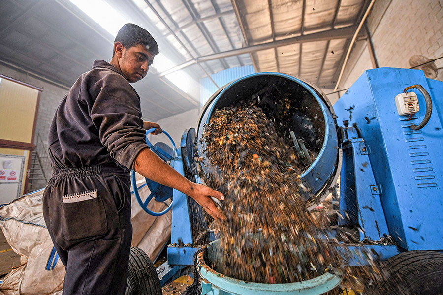 A worker dumps plastic waste out of a mixer before it is to be recycled into eco-friendly interlocking tiles used in outdoor walkways at a workshop of the startup company 