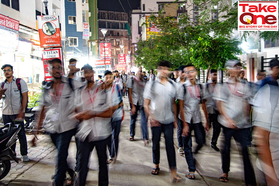 Student walking past posters displaying 1st rankers for various coaching institutes in Kota