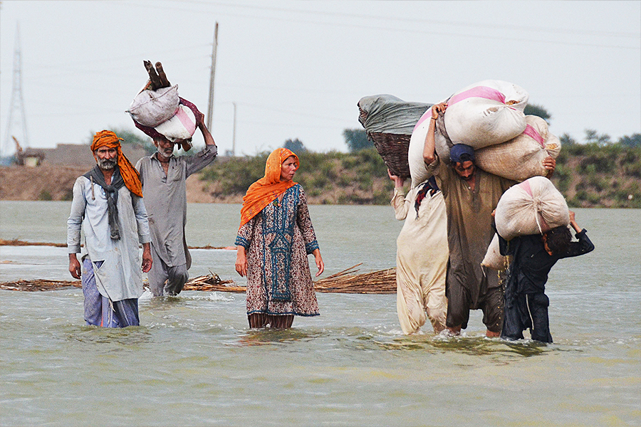 Villagers carrying animal feed wade through flood waters following monsoon rainfalls in Jaffarabad district in Balochistan province on August 24, 2022. - Record monsoon rains were causing a 