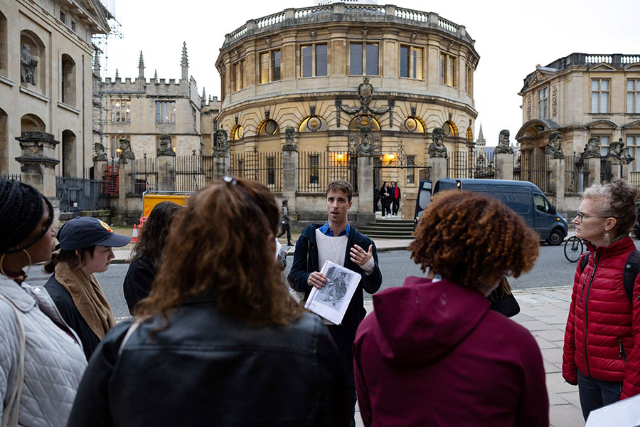 Tour guide Oliver talks with a group of people attending an 'Uncomfortable Oxford' tour outside the Sheldonian Theatre on Broad Street, in Oxford. 
Image: Henry Nicholls / AFP©