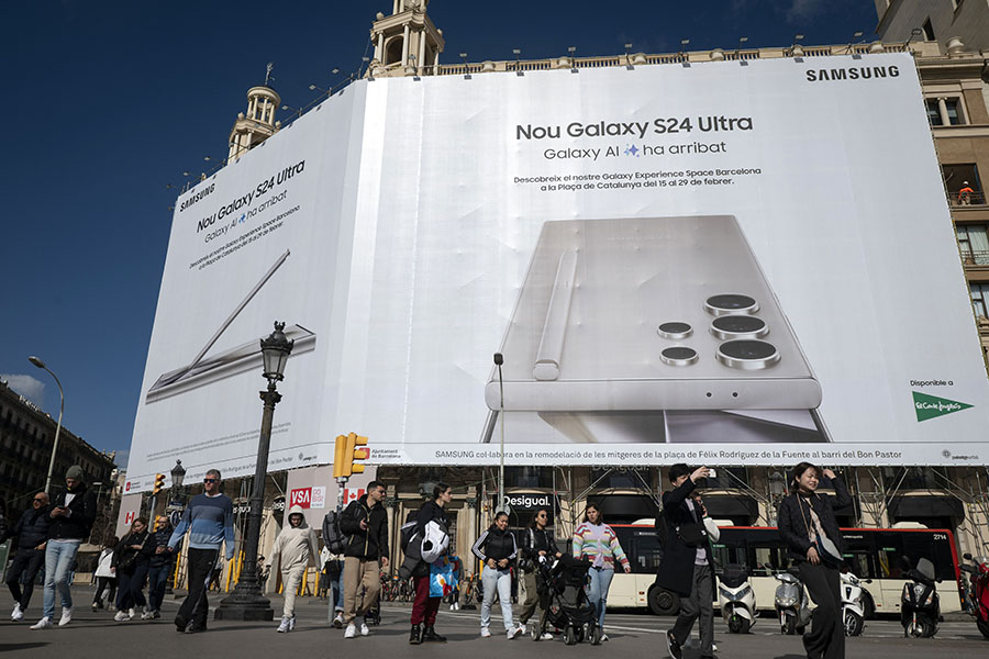 People walk past a building wrapped in an advertising banner, ahead of the Mobile World Congress (MWC), in Barcelona on February 23, 2024. Image credit: Josep LAGO / AFP