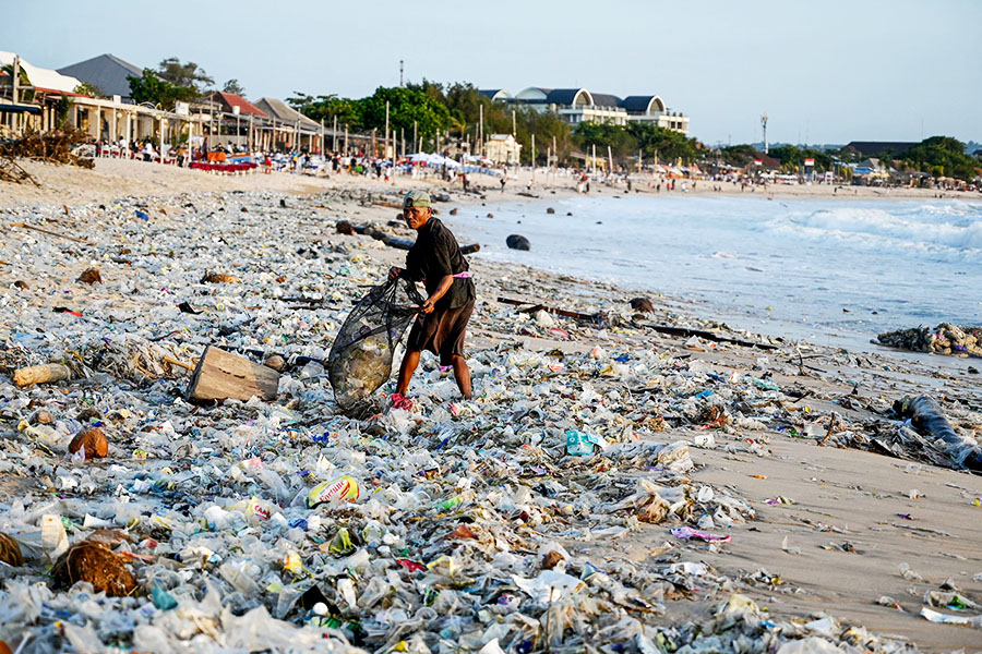 A man collects recyclable items to sell amid plastic and other debris washed ashore at Kedonganan Beach near Denpasar on Indonesia's resort island of Bali on March 19, 2024. Image: SONNY TUMBELAKA / AFP©
