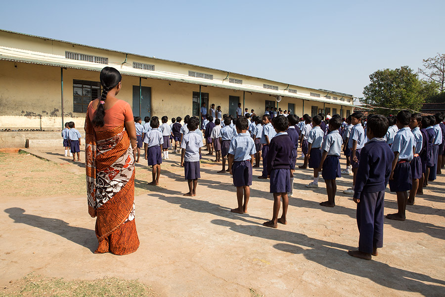 Karon, India - March 07, 2013: Several school boys and girls are standing in line while a female teacher in a orange sari is watching them. (Photo by Christian Ender/Getty Images)